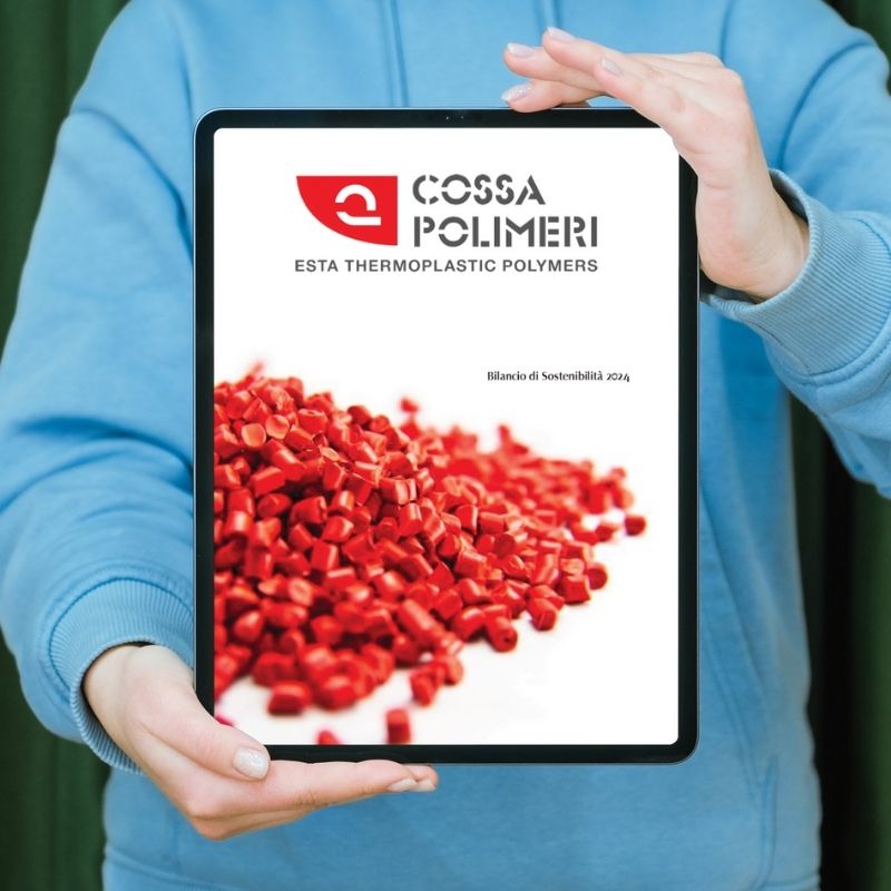 Una persona tiene in mano un tablet con la copertina del Bilancio di Sostenibilità 2024 di Cossa Polimeri, che mostra granuli rossi in primo piano.